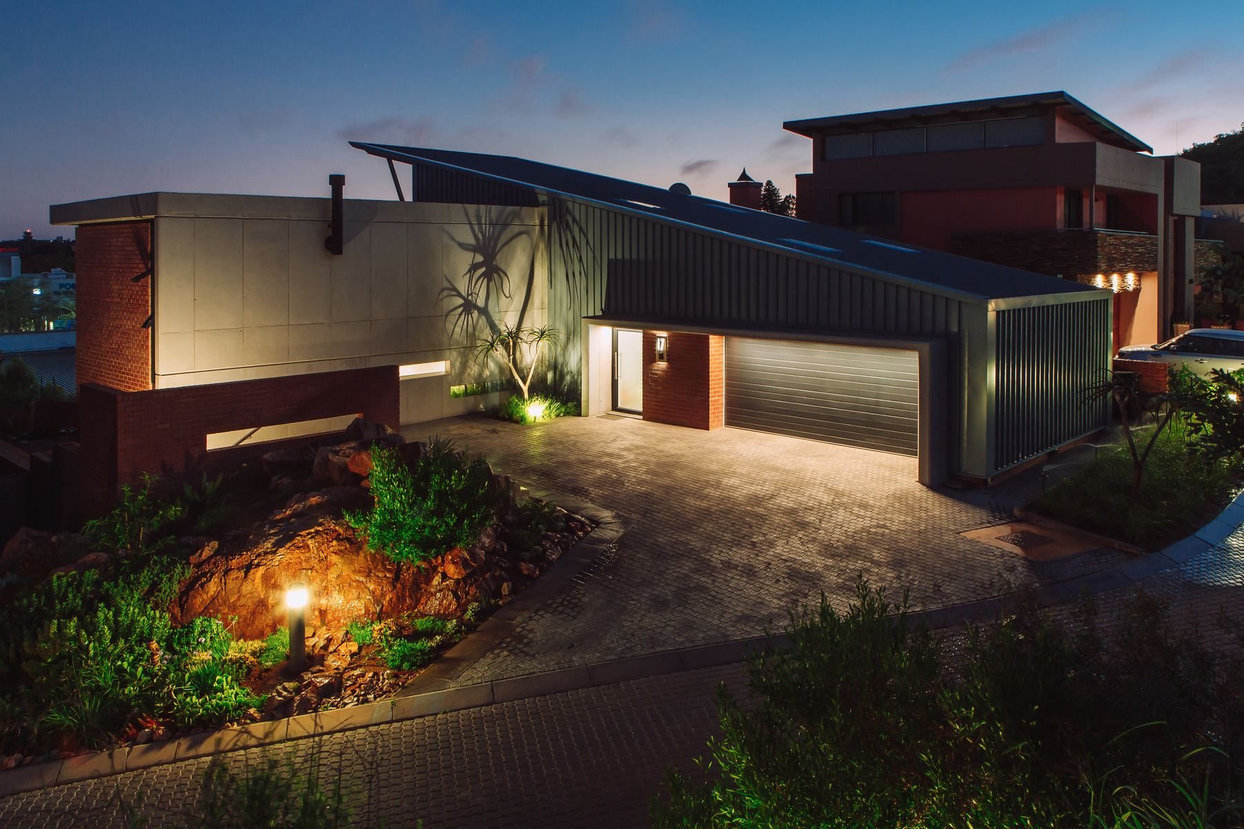 Contemporary house at dusk with a sloping green roof, a lit garden and a rock outcrop in the foreground.