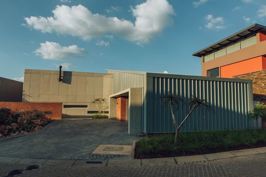 House with an entrance courtyard, a clad garage volume and a landscaped garden under a partly cloudy sky.