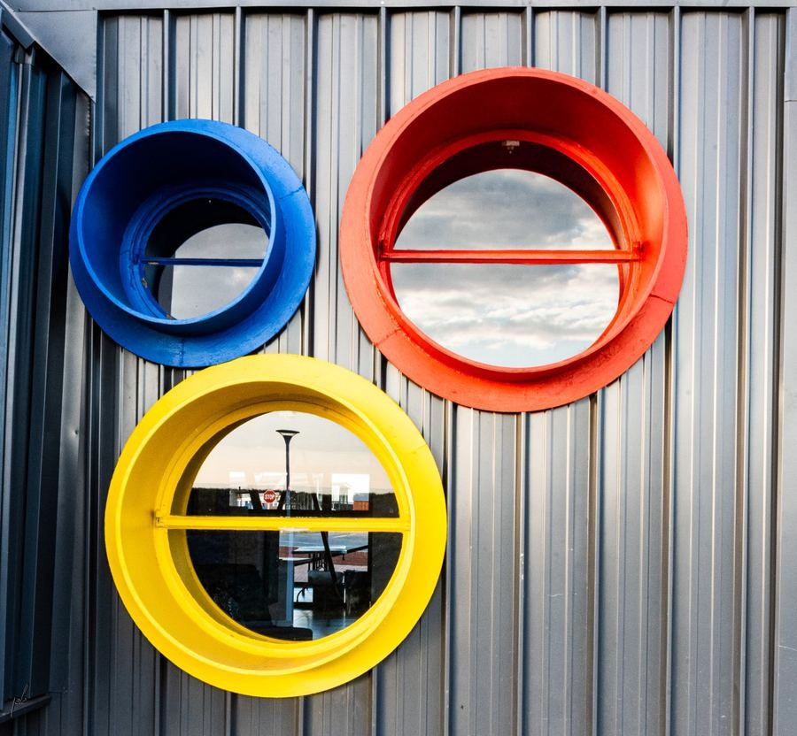 Close view of blue, red and yellow circular windows set in corrugated steel cladding.