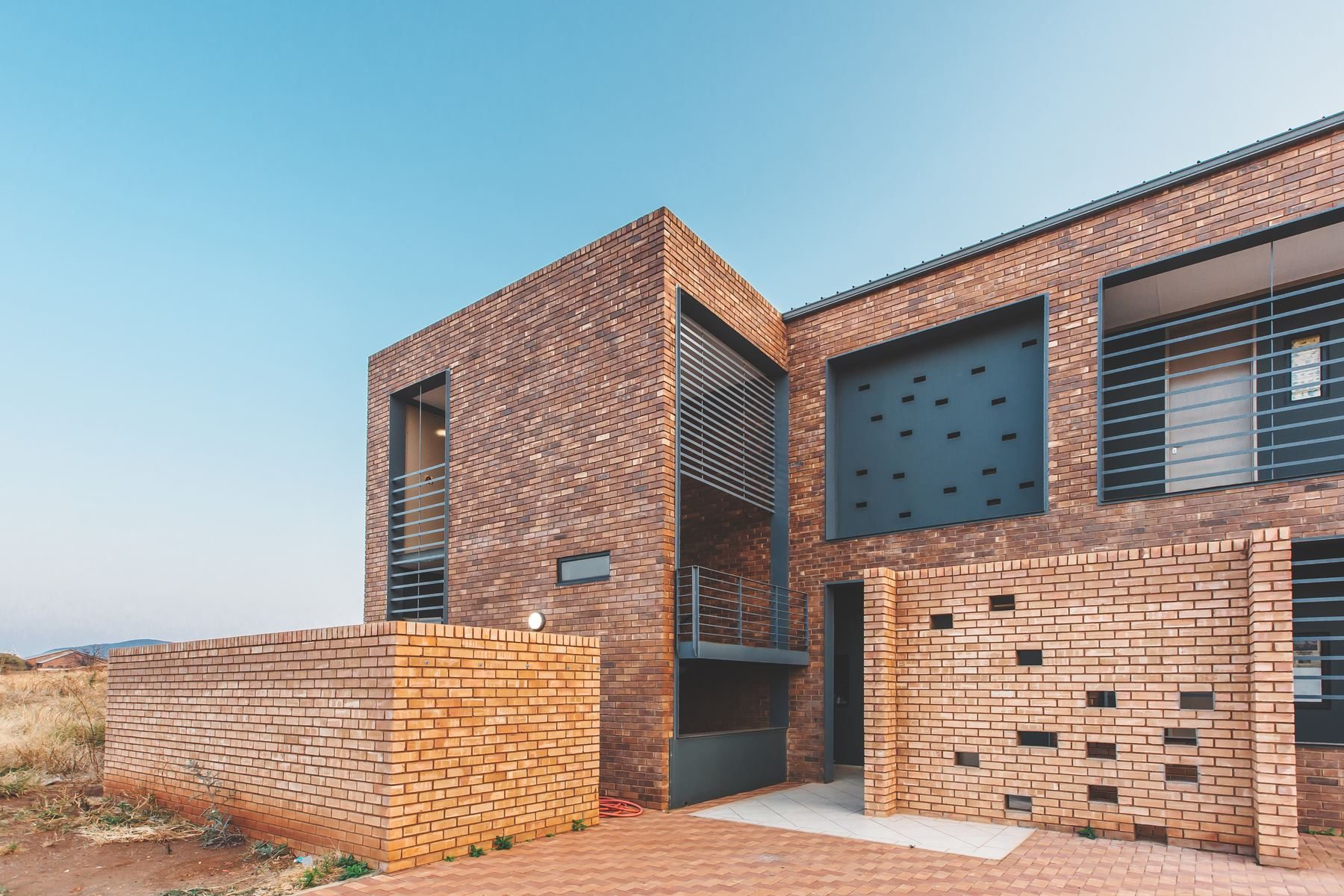 Two-storey face-brick housing units with steel louvre screens and a perforated brick wall, at dusk.