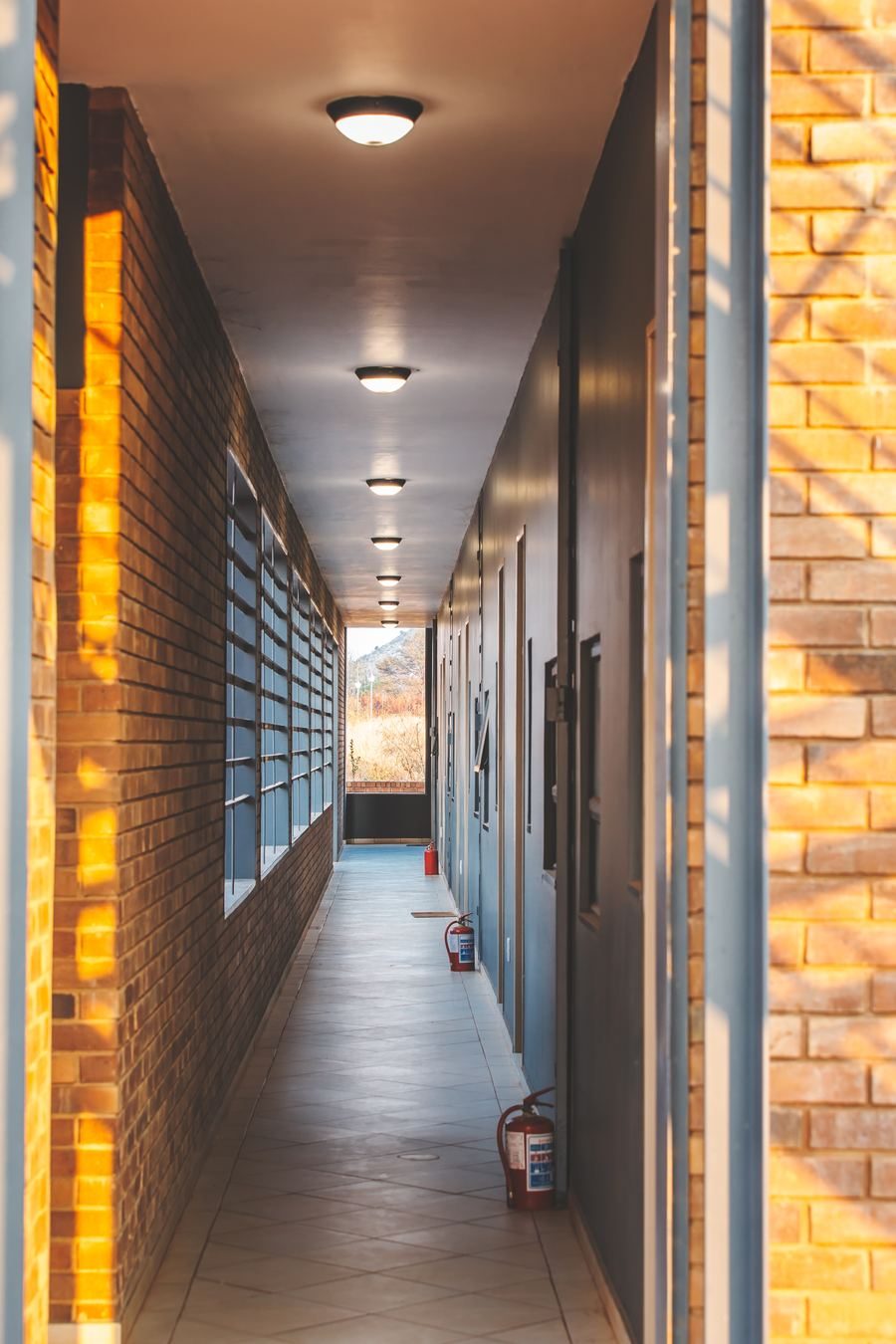Access corridor with face-brick walls and louvred windows, with a view of the mountains at its end.