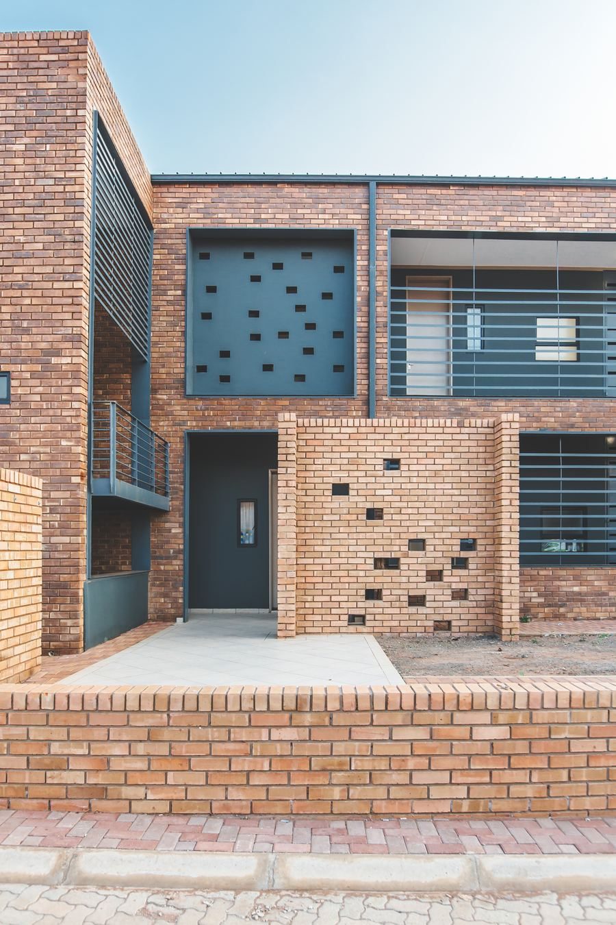 Ground-floor frontage of a housing unit with a perforated brick screen wall and a dark steel door.